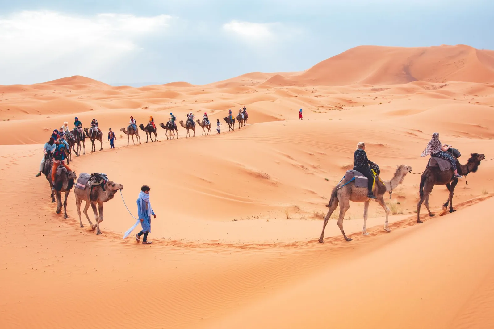 Caravana de dromedarios con visitantes entre las dunas anaranjadas de Merzouga