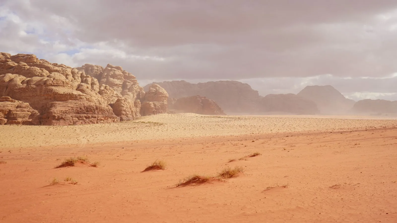 Paisaje rojo de Wadi Rum con formaciones de arenisca al fondo y arena en primer plano